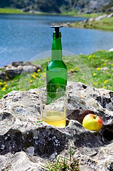 Green bottle and glass of natural Asturian cider made fromÂ fermented apples with view on Covadonga lake and tops of Picos de